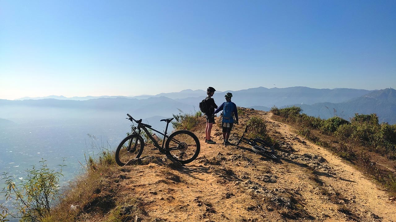 Mountain bikers enjoying the view of Pokhara valley with their bikes parked aside.