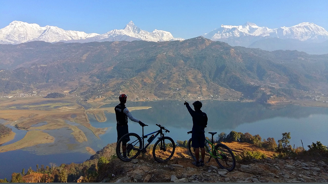 A mountain bike guide is pointing out the name of the mountain to his guest.