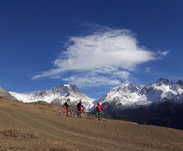 Mountain bikers riding the Lupra single track of Mustang and the view of Thorong Peak and Mukti Himal is on the background.
