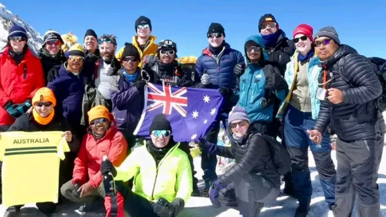 Group of mountain bikers on top of Thorong-La pass posing for a picture with the flag of Australia.