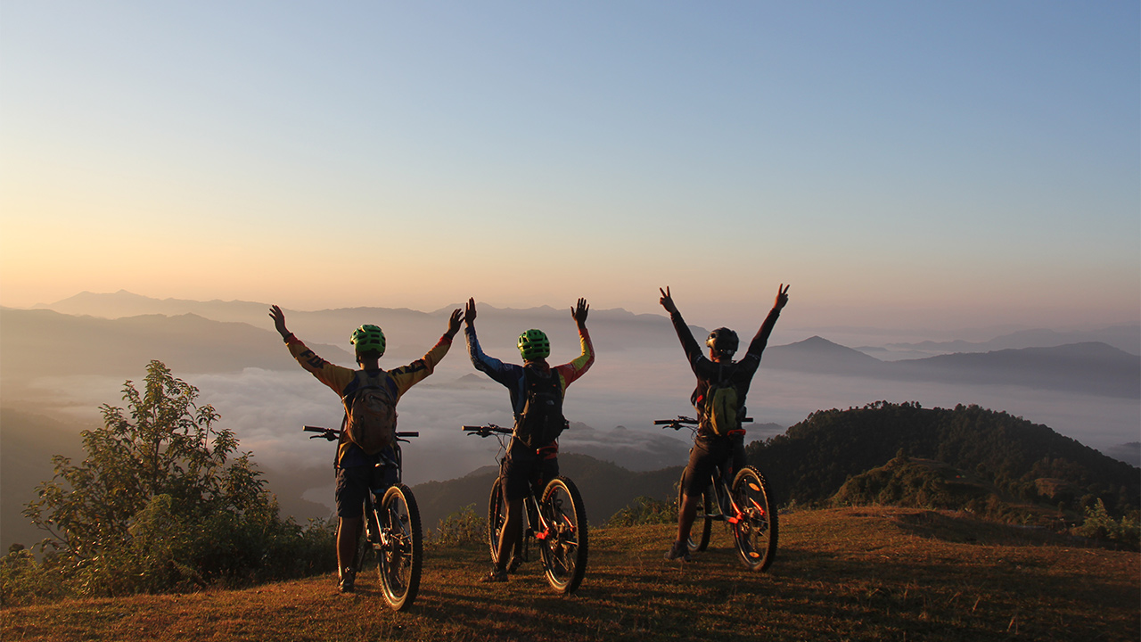Three mountain bikers raising their hands to cherish the beautiful sunrise.
