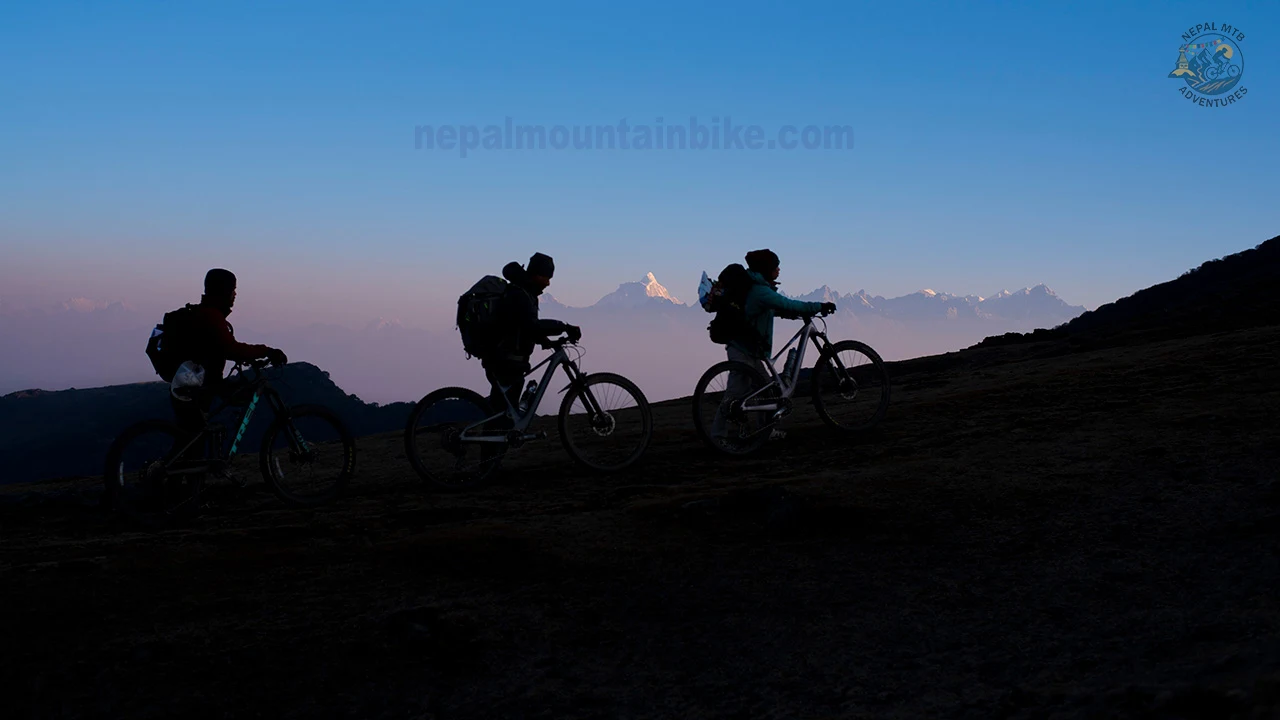 Three mountain bikers pushing bikes to catch the sunrise view over Everest during Pikey Peak mountain biking tour in the Himalayas of Nepal.