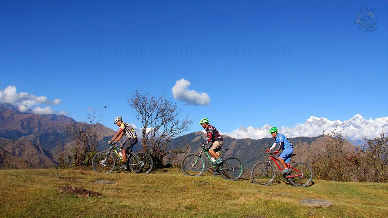 Mountain bikers are riding their bikes in a single line with the backdrop of the Himalayas during the Kathmandu to Pokhara mountain bike tour in Nepal.