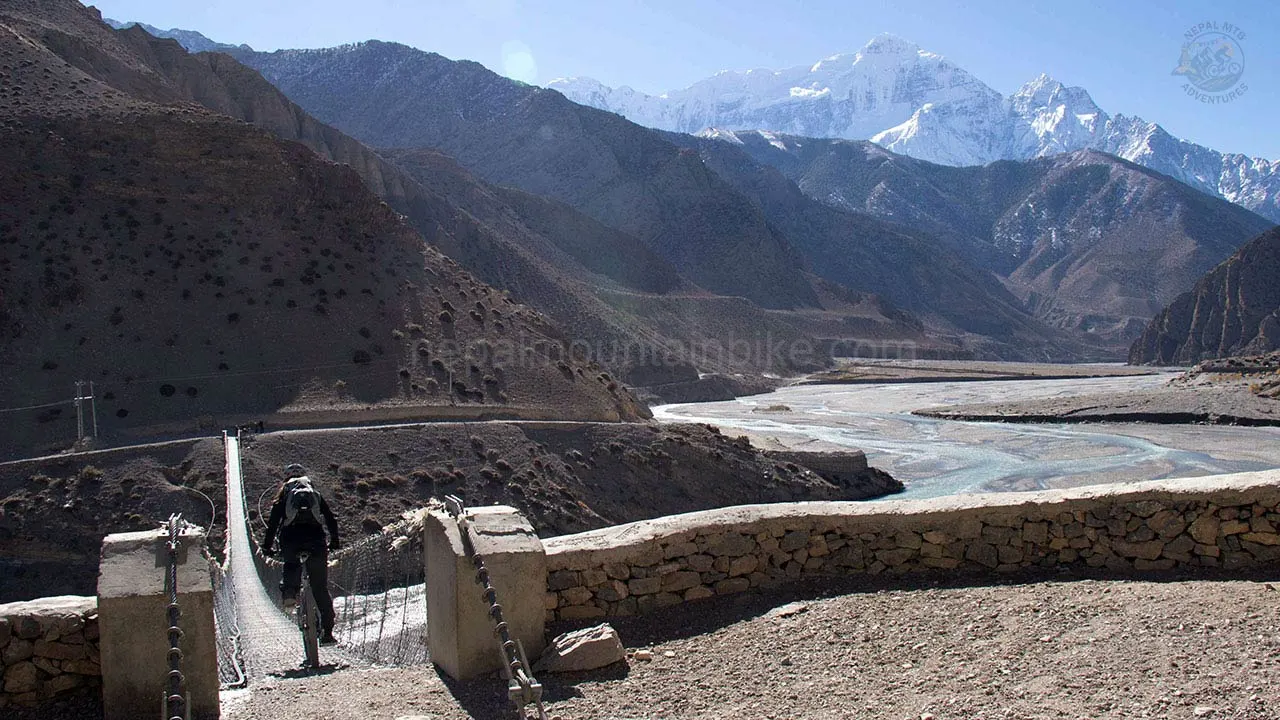 A mountain biker crosses the suspended bridge over Kali Gandaki River during Lower Mustang XC mountain bike tour in Nepal.
